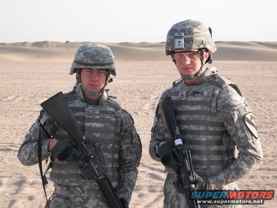 Two soldiers in desert camouflage uniforms and helmets stand in a sandy, desert landscape. One soldier's name tag reads 'FERGUSON', the other's reads 'DAVIS'. Both hold rifles