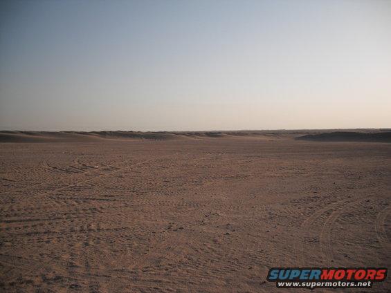 Vast desert landscape with tire tracks in the sand under a clear sky