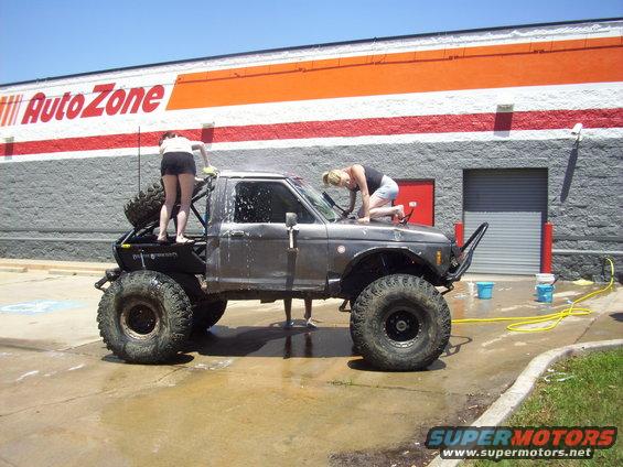 Modified off-road truck with large tires being washed in front of an AutoZone