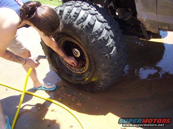 person spraying water on a huge mud tire and wheel, cleaning off dirt