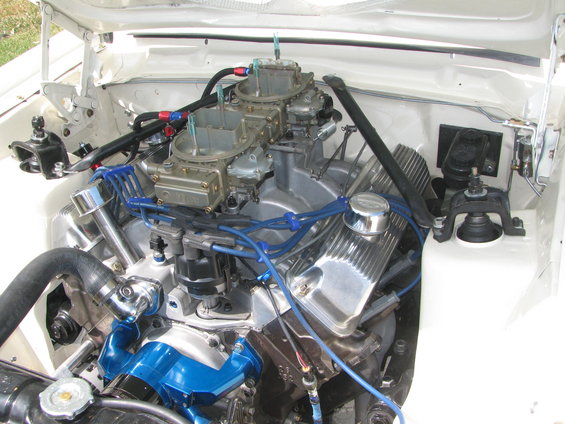 White vehicle engine bay with dual carburetors, chrome valve covers, and blue spark plug wires