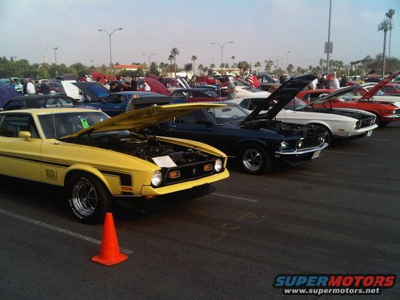 Yellow 1971 Ford Mustang Mach 1 with hood open, parked in a lot with other classic cars