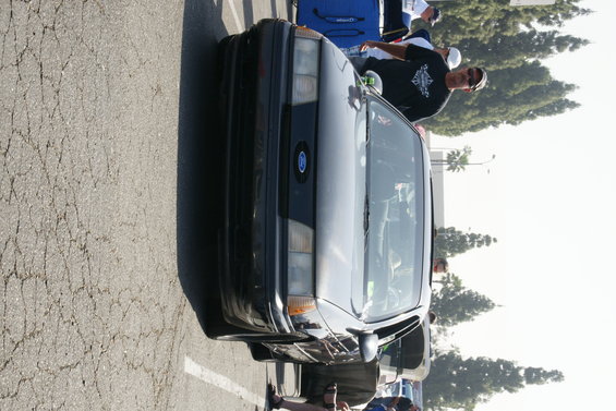 Black 1992 Ford Taurus parked outside, front view. People are standing around it