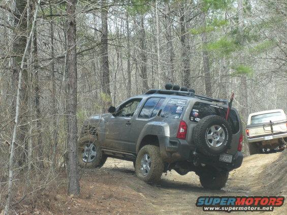 Gray Nissan Xterra driving on a dirt trail in woods, with another vehicle behind it