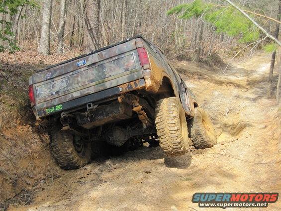 Camouflaged Ford Bronco climbing a muddy hill, rear view