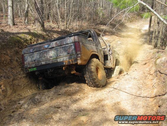 Camouflaged off-road SUV climbing a muddy hill, kicking up dirt