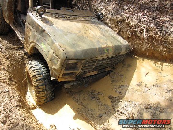 Muddy off-road vehicle with front tire deep in a ditch, stuck in mud