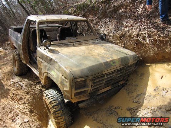 Mud-covered 1980 Ford Bronco stuck in a muddy ditch, front 3/4 view
