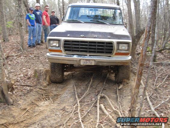 Ford F-Series truck on a dirt trail with trees around. Four guys stand behind it