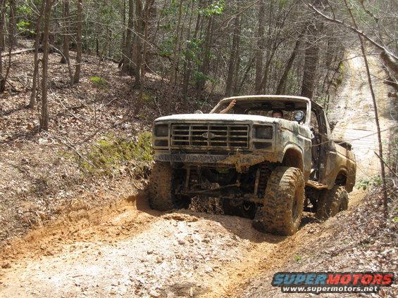 Mud-covered 1980 Ford F-Series truck on a dirt trail, front view