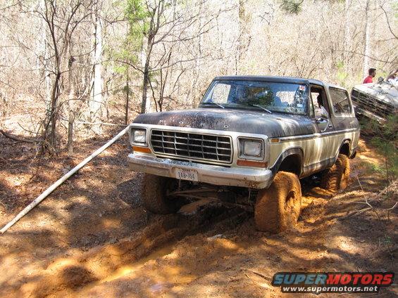 Mud-covered 1978 Ford Bronco stuck in dirt with another vehicle partially visible behind it
