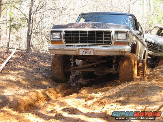Front view of a lifted 1978 Ford Bronco driving through mud