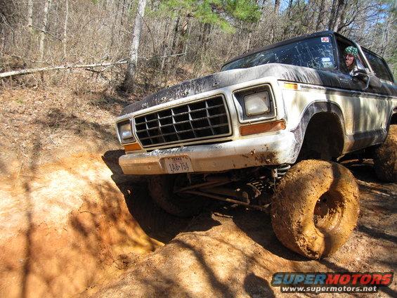 Ford Bronco climbing over mud and rocks on a trail. Driver visible