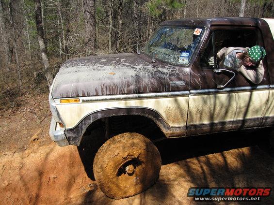Brown and tan 1978 Ford Bronco with mud-caked tire, driver visible