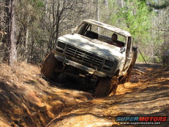 White Ford pickup truck climbing a muddy hill with trees around