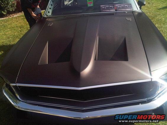Dark matte hood with a large scoop and chrome grille on a car