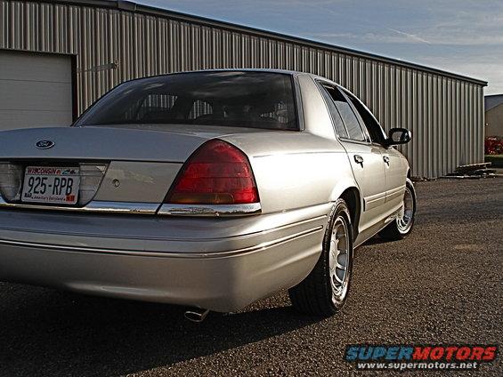Silver 2000 Ford Crown Victoria sedan, rear quarter view, parked on gravel in front of a corrugated metal building