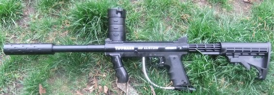 Paintball gun with 'TIPPMANN 98 CUSTOM' text on it, lying on grass