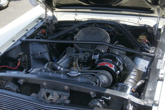 Engine bay of a white car with a black air cleaner and hoses. Some text is visible on a label