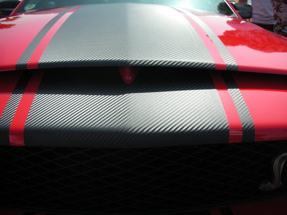 Red car hood with gray carbon fiber stripes and red pinstripes. Grille visible below