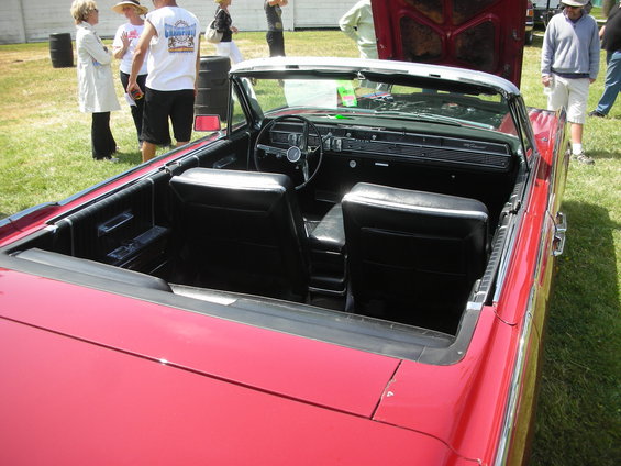 Red convertible interior with black seats and dashboard. People are visible in the background