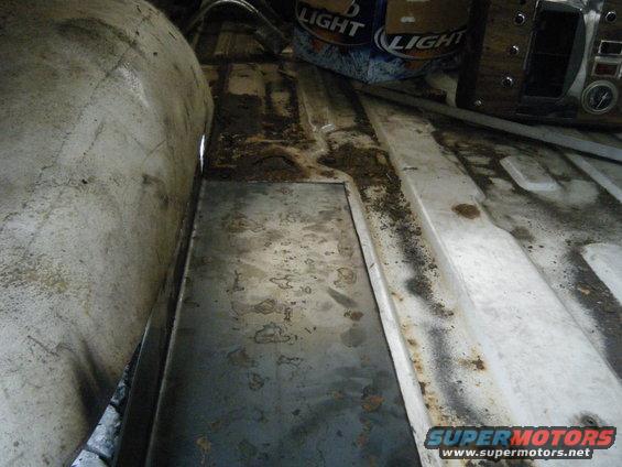 Interior floor of a vehicle with a patch of metal installed, showing dirt and rust
