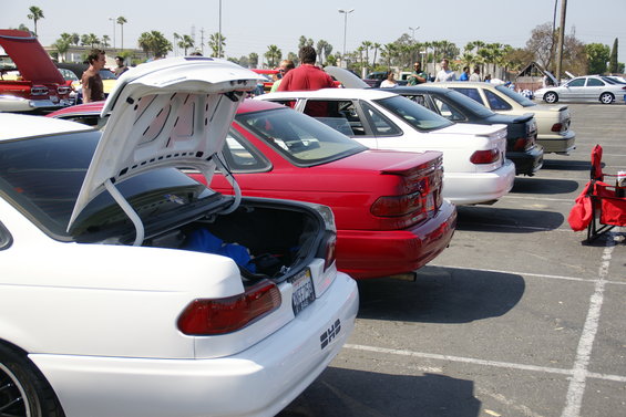 White sedan with trunk open, red sedan, and other cars parked in a lot