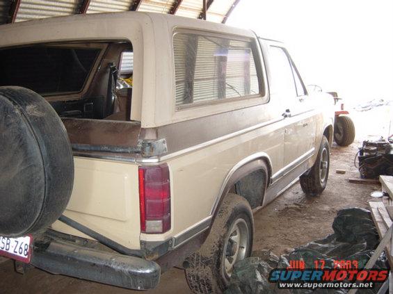 Tan and brown Ford Bronco with a spare tire mounted on the rear, seen from the back-left
