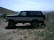 1994 Ford Bronco - A lifted Ford Bronco sits parked on a dry, grassy hillside under a clear blue sky.