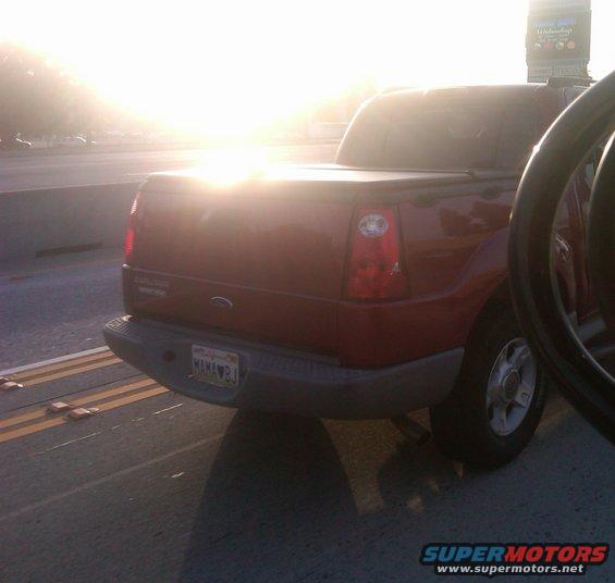 Red pickup truck rear with soft tonneau cover and California license plate reading MAMAWBJ