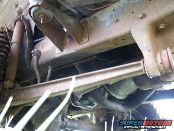 Underside view of vehicle suspension and frame components. Tire tread visible