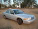 2003 Ford Crown Victoria - A silver 2003 Ford Crown Victoria is parked on a gravel lot with trees in the background.