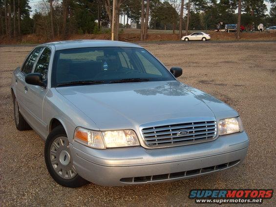 Silver 2003 Ford Crown Victoria parked on gravel lot. Another car is visible in the background