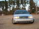 2003 Ford Crown Victoria - Front view of a silver 2003 Ford Crown Victoria parked on a gravel lot with trees in the background.