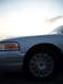 2003 Ford Crown Victoria - The front quarter panel and wheel of a silver Ford Crown Victoria are visible under a bright sky.