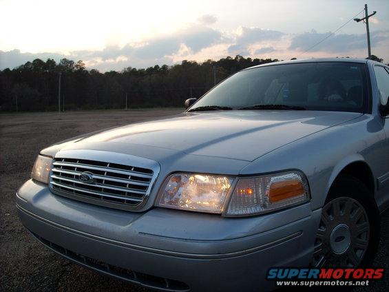 Silver 2003 Ford Crown Victoria front grille and headlights under a cloudy sky