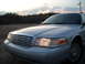 2003 Ford Crown Victoria - The front end of a silver 2003 Ford Crown Victoria is visible under a dusky sky.