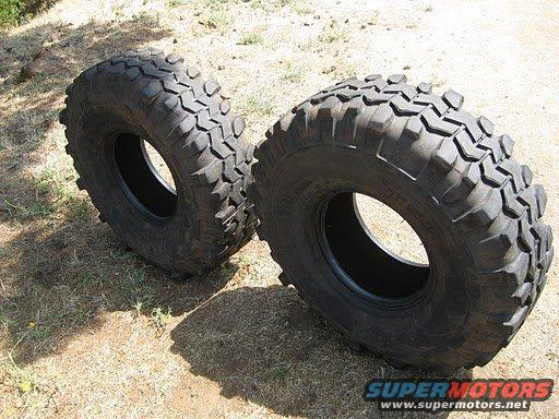 Two large off-road tires with aggressive tread patterns sit on dry ground