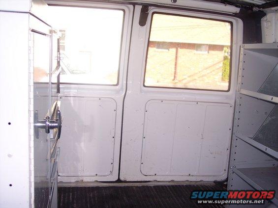 Interior of a white van showing two doors, shelving, and a metal handle