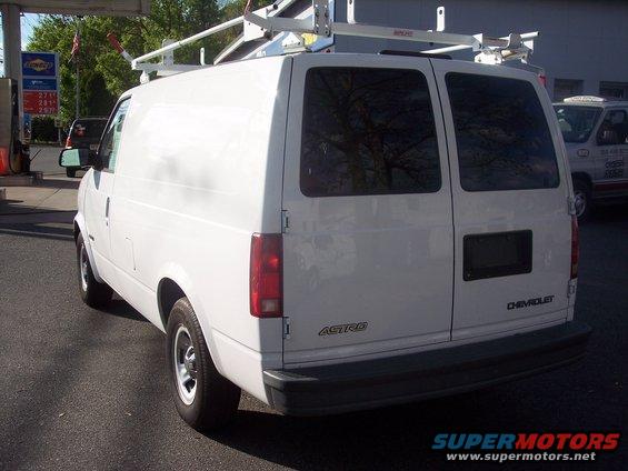 White Chevrolet Astro van with a ladder rack, seen from the rear at a gas station