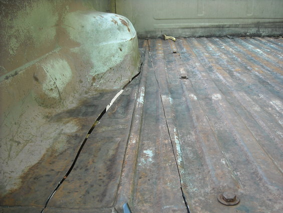 Close-up of a heavily rusted truck bed floor and a cracked, rounded fender well. The metal shows significant wear and tear