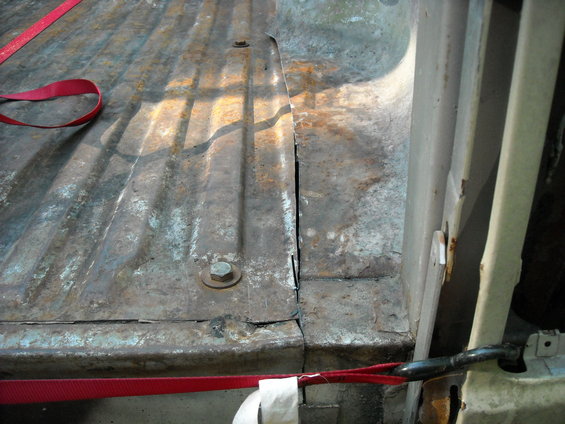 Rusty truck bed with a red strap. A seam in the metal is visible