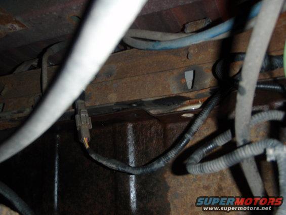 Underside of a vehicle showing rusty frame rails and various electrical wires and connectors