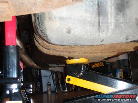 Undercarriage of a vehicle supported by red jack stands and a yellow hydraulic jack, with a DeWalt tool box visible