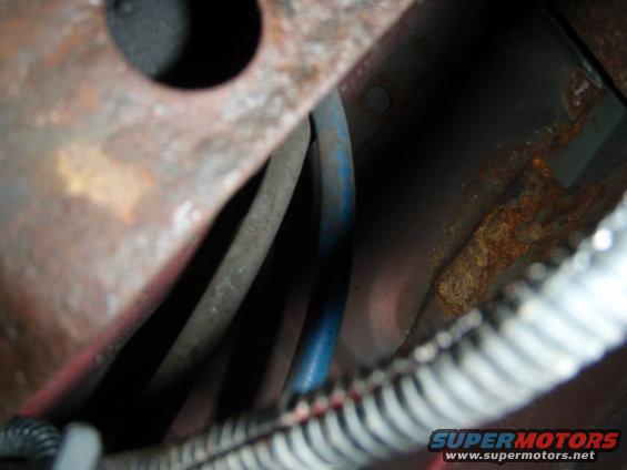 Close-up of rusted metal and blue and gray wires, with a corrugated conduit