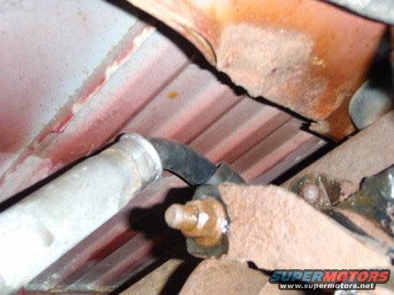 Underside of a vehicle showing rusty metal, a pipe, and a bolt