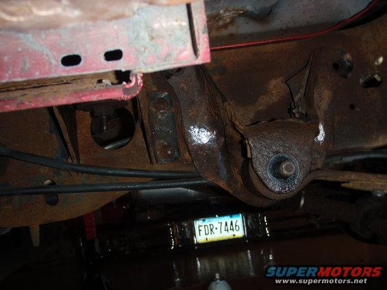 Close-up of heavily rusted vehicle frame and suspension parts, with a license plate visible underneath