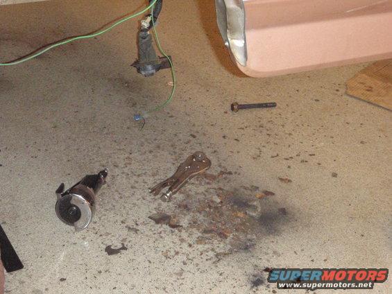 Vehicle part, vise grips, and bolt on concrete floor near a pink vehicle panel