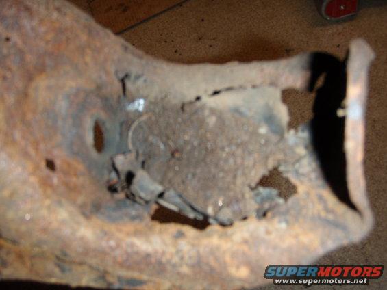 Heavily rusted metal suspension component with a large hole