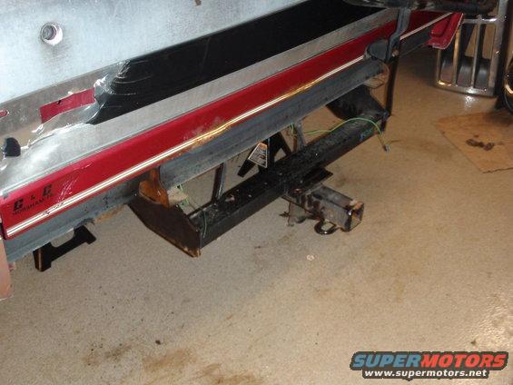 Rear bumper with red stripe and black trim, trailer hitch, and visible suspension components